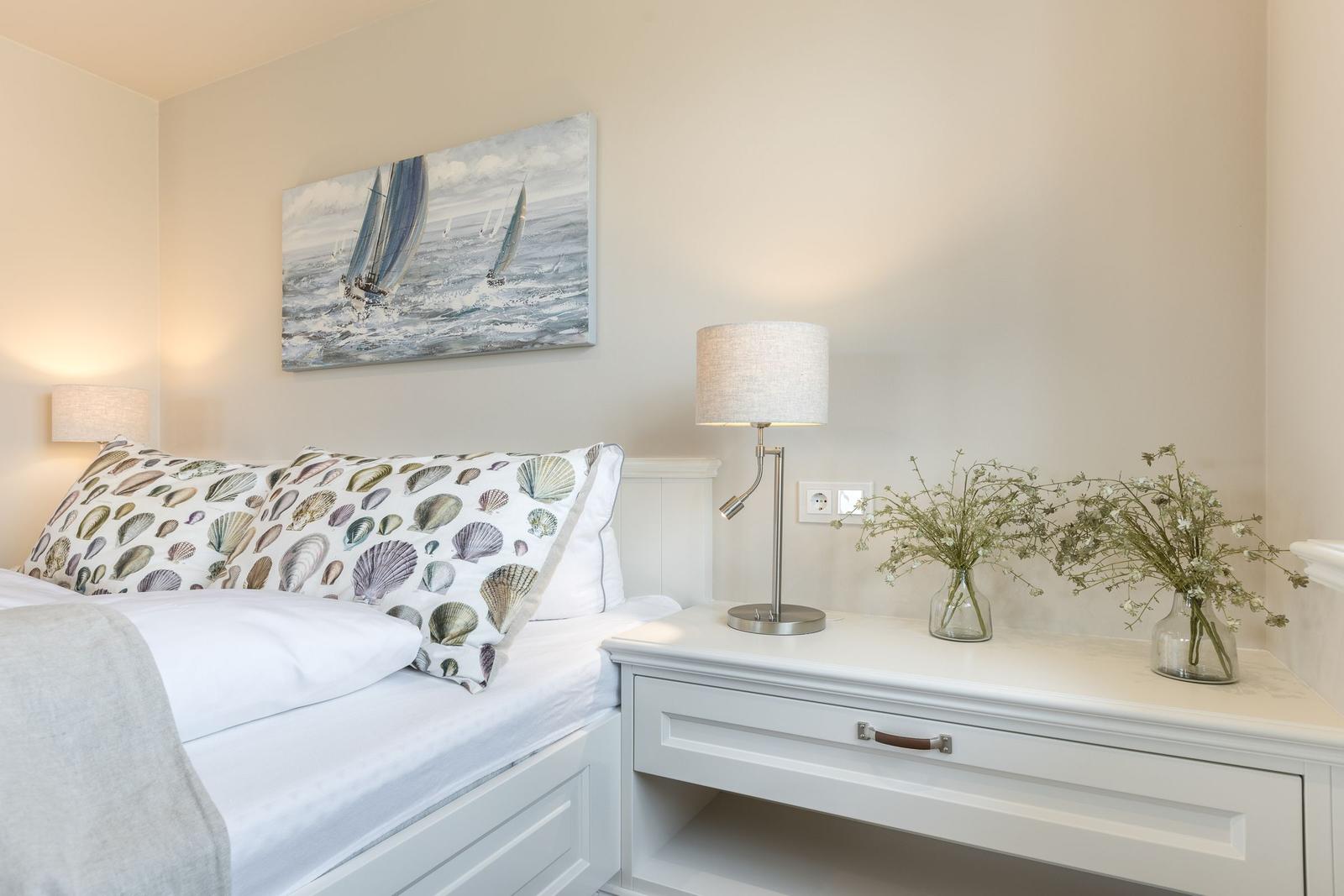 Schlafzimmer mit Bett, Nachttisch und Wandbild mit Segelbooten.