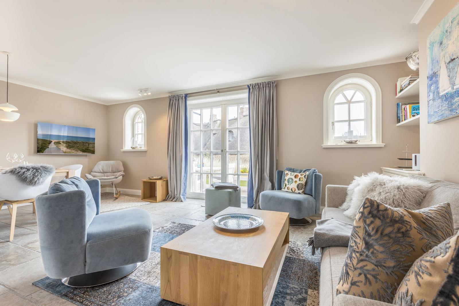 Wohnzimmer mit Sofa, Sessel und Holztisch. Fenster mit Vorhängen und Wandbild.