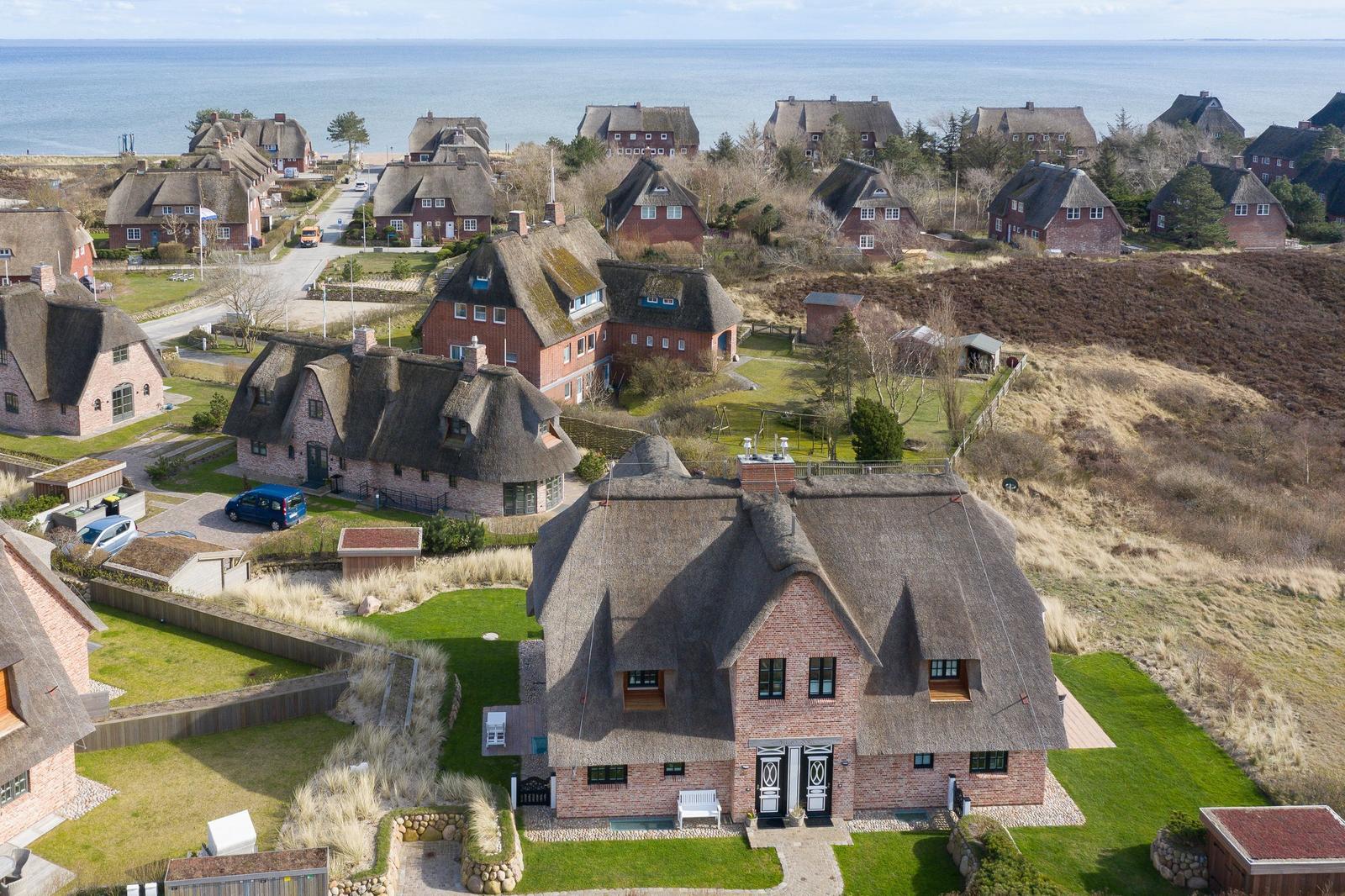 Dorfhaus mit Strohdach und Garten, Blick auf Meer und umliegende Häuser.