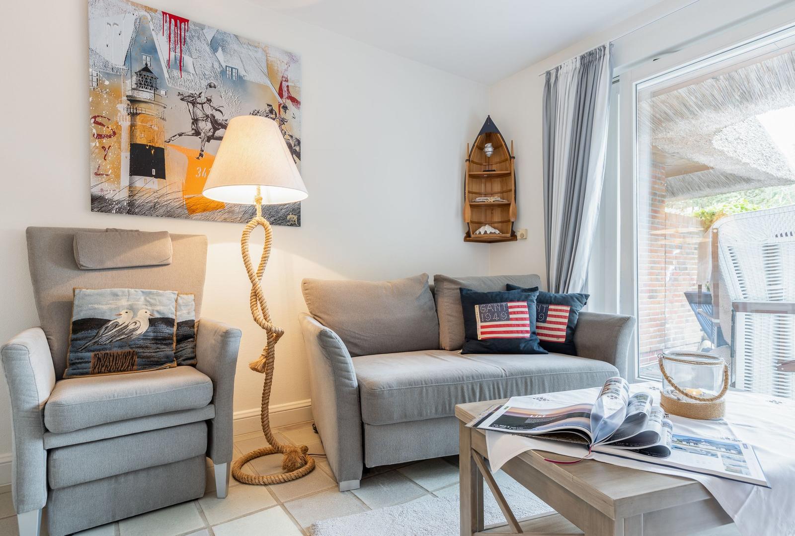 Wohnzimmer mit Sofa, Sessel und Tisch. An der Wand hängt ein Bild und eine hölzerne Bootswand. 