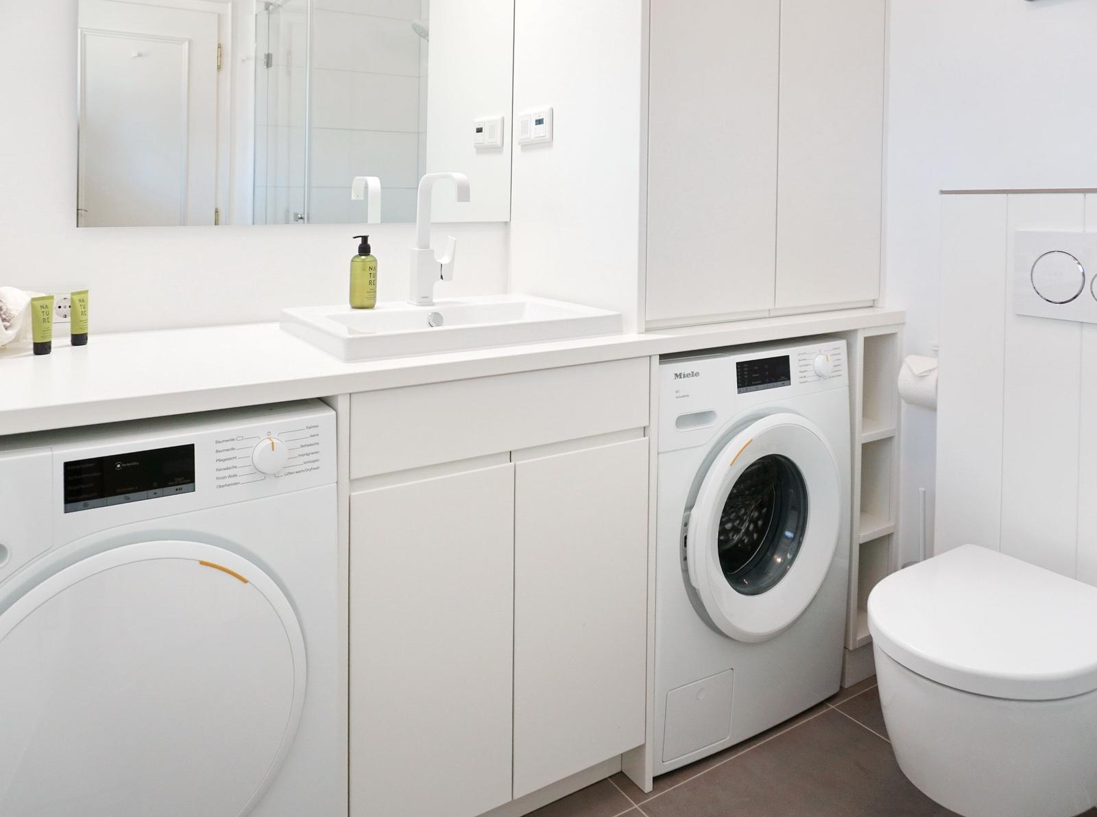 Badezimmer mit Waschmaschine, Spülmaschine und Toilette.