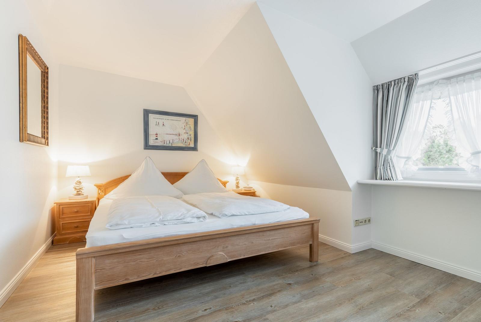 Schlafzimmer mit Dachschrägen, Holzbett und Fenster mit Vorhängen.