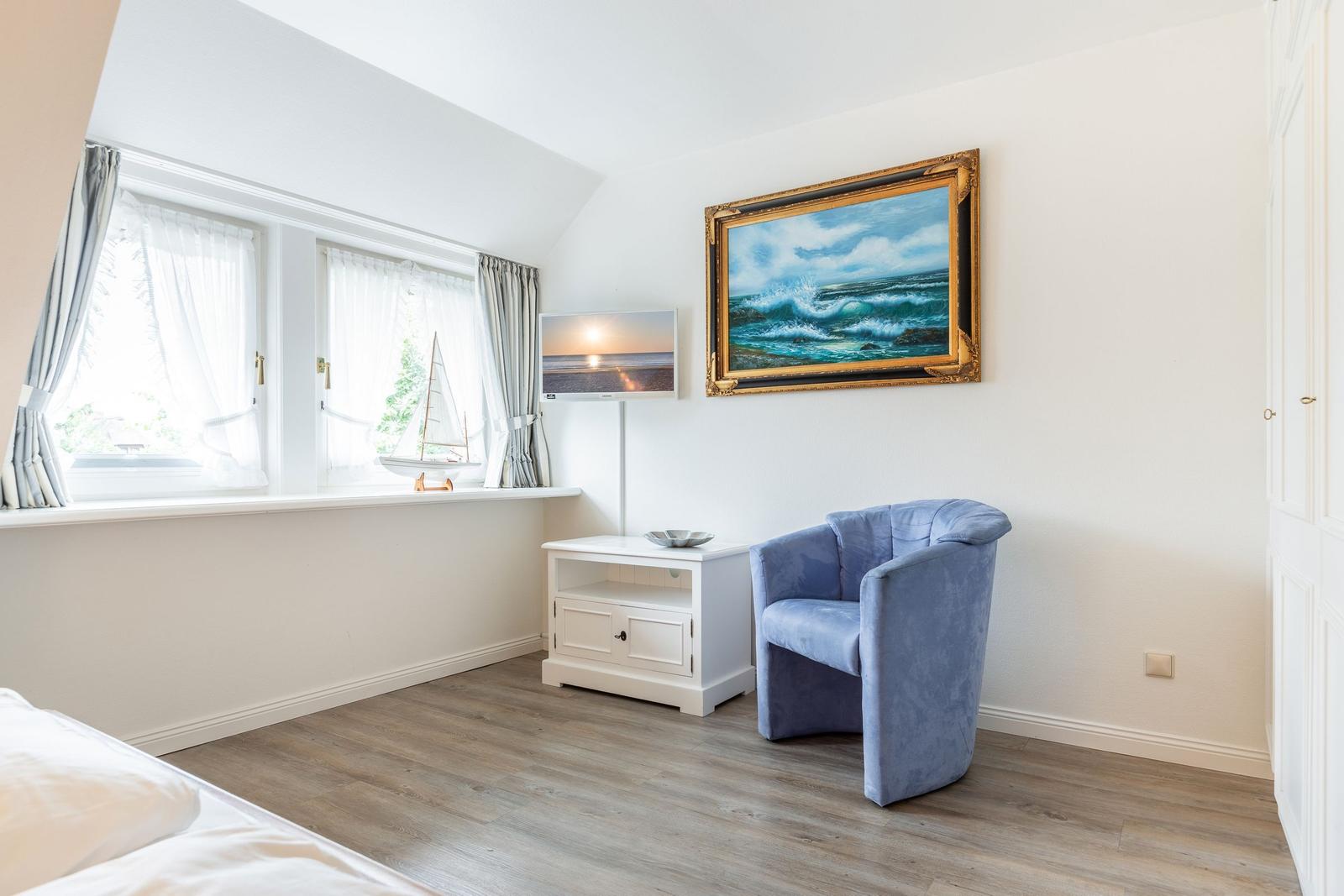 Zimmer mit blauem Sessel, Wandbild und Fenster mit Segelbootmodell.