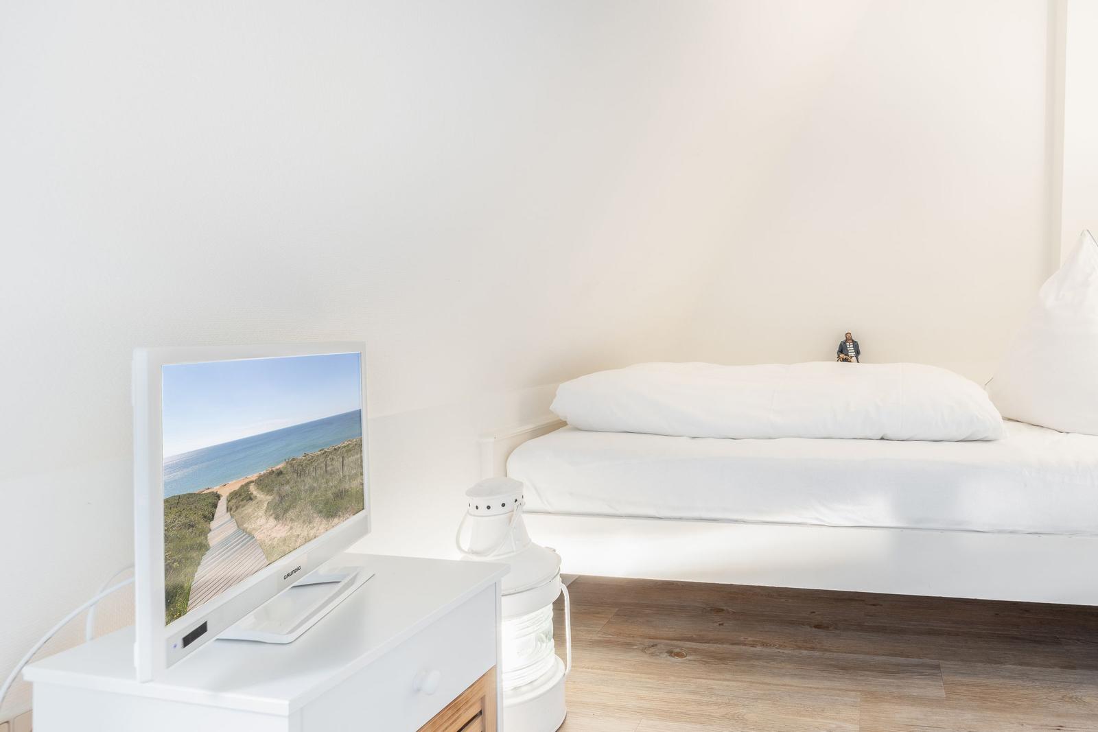 Schlafzimmer mit weißem Bett und Fernseher auf Nachttisch.