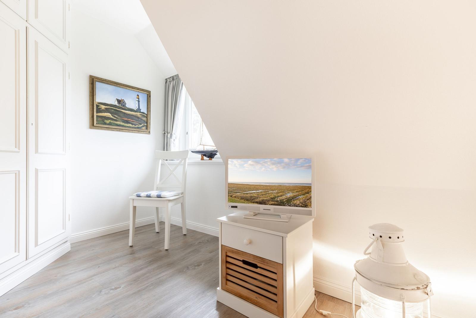 Zimmer mit Schrank, Stuhl, Fernseher und Laterne unter Dachschräge