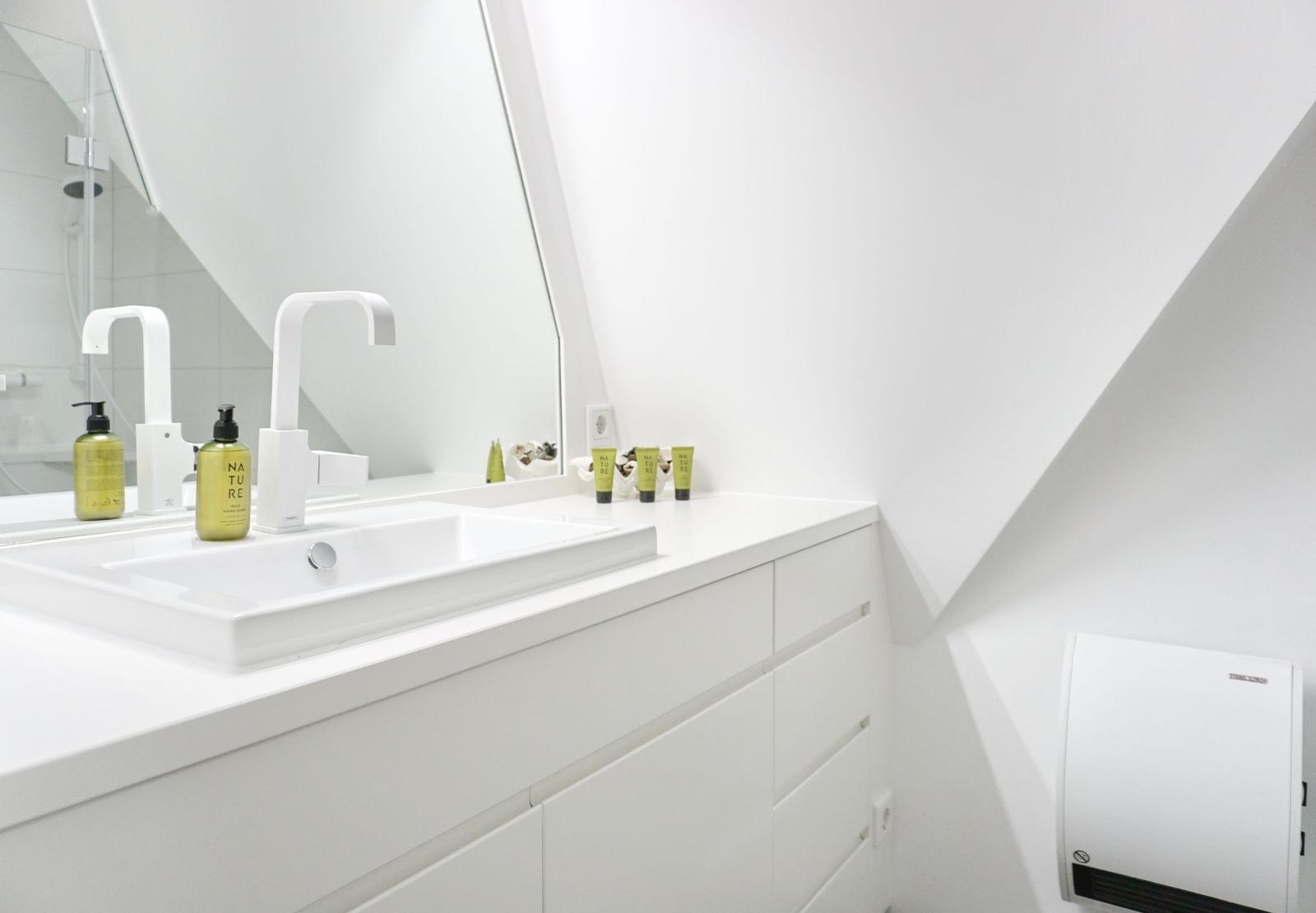 Weiße Dusche mit modernem Waschbecken und Spiegel. Dachboden-ähnliche Decke.