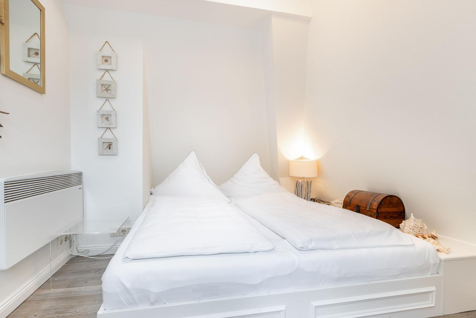 Schlafzimmer mit weißem Bett, Nachttisch und Wanddekoration.