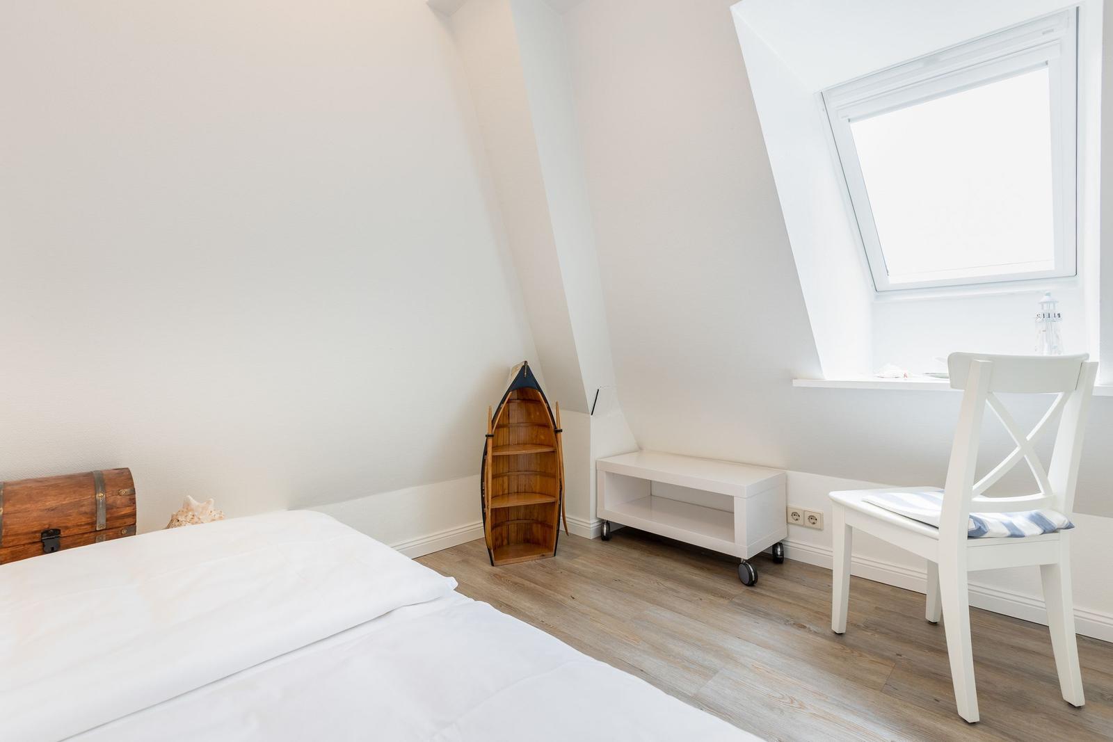 Schlafzimmer mit Dachschrägen, Bett, Stuhl und Fenster