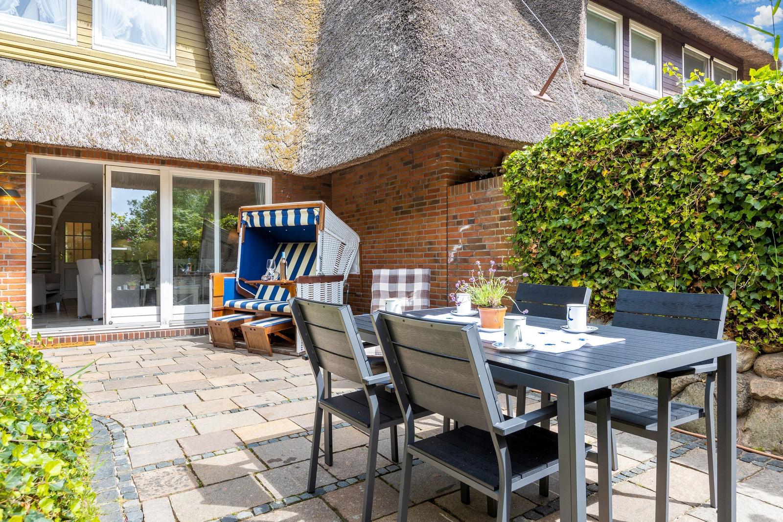 Terrasse mit Tisch, Stühlen und Strandkorb vor einem Haus mit Strohdach.