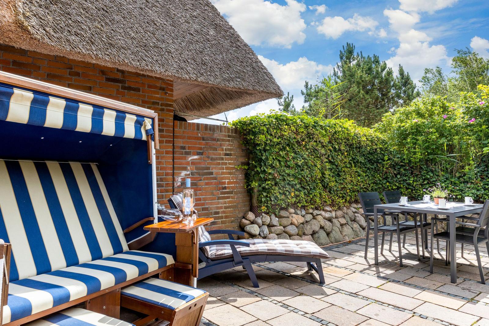 Terrasse mit Strandkorb, Tisch und Stühlen. Hinterhof mit Hecke und Steinmauer.