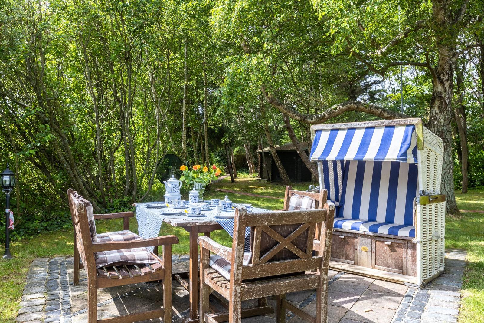 Garten mit Tisch, Stühlen und Strandkorb unter Bäumen.