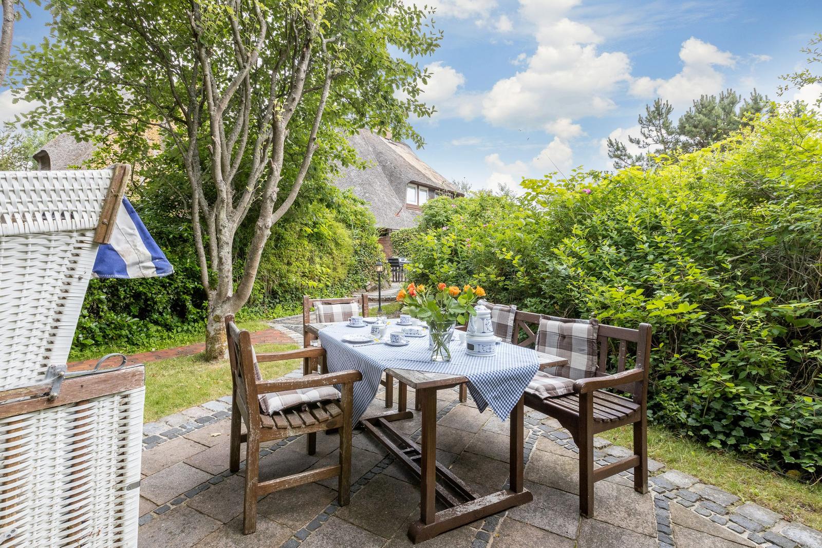 Hinterhof mit Tisch, Stühlen und Blumen. Hintergrund: Haus mit Schindeldach.