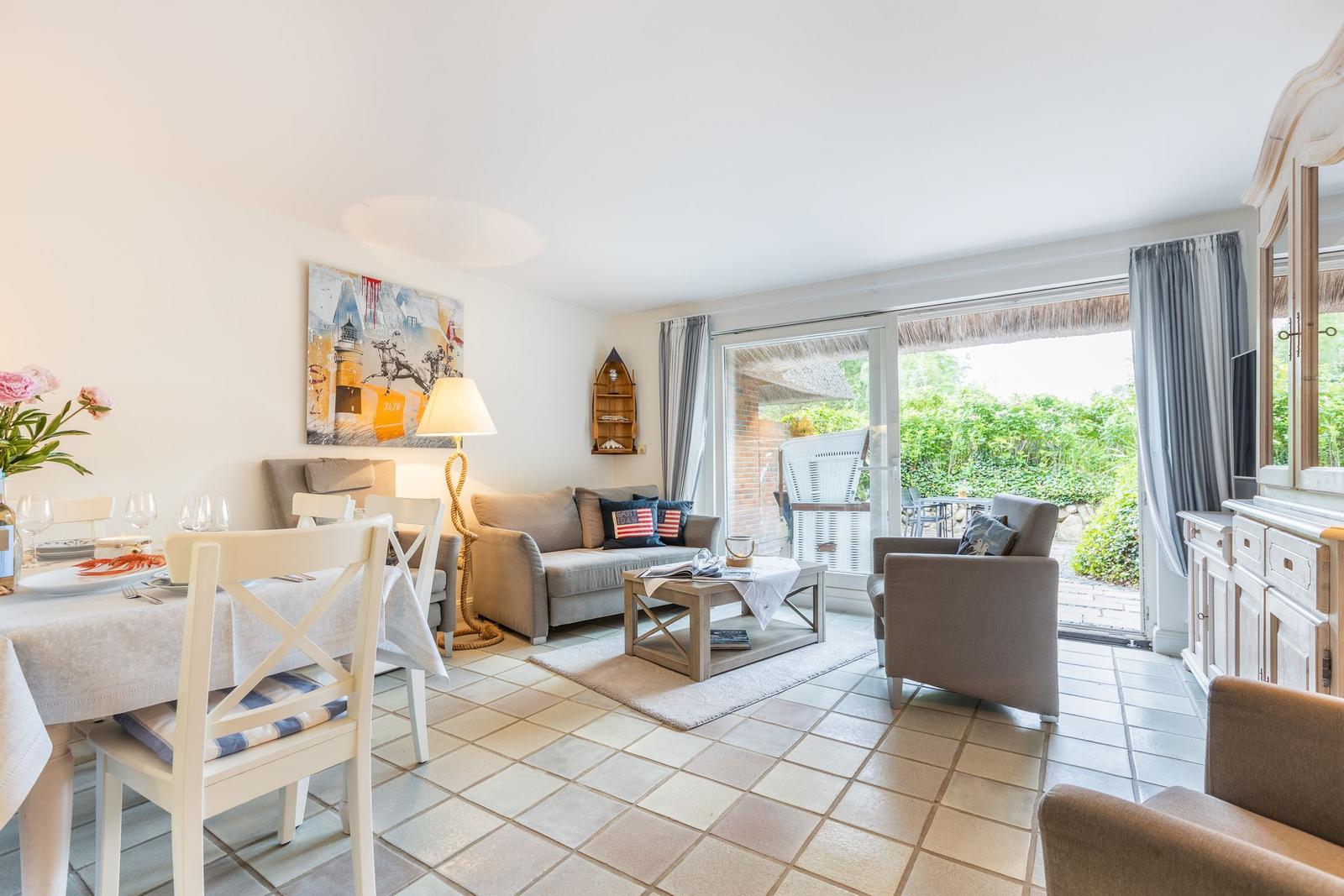 Wohn- und Essbereich mit Terrasse, Sofa, Stühlen und Tisch. Wandbild und Gardinen sichtbar.