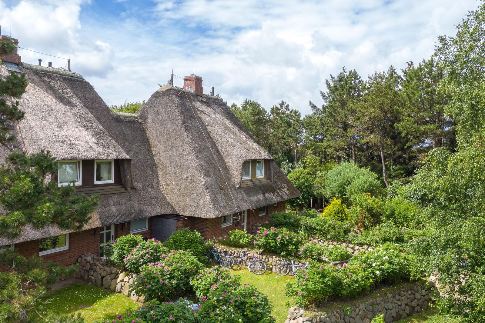 Haus mit Strohdach, Garten mit Blumen und Fahrräder.