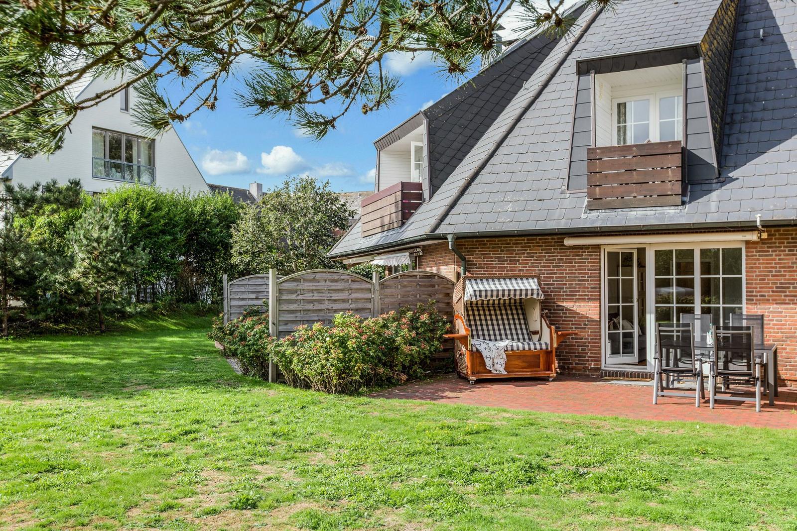 House with balcony, garden, and lounge chair. Terrace with table and chairs. Backyard with wooden fence.