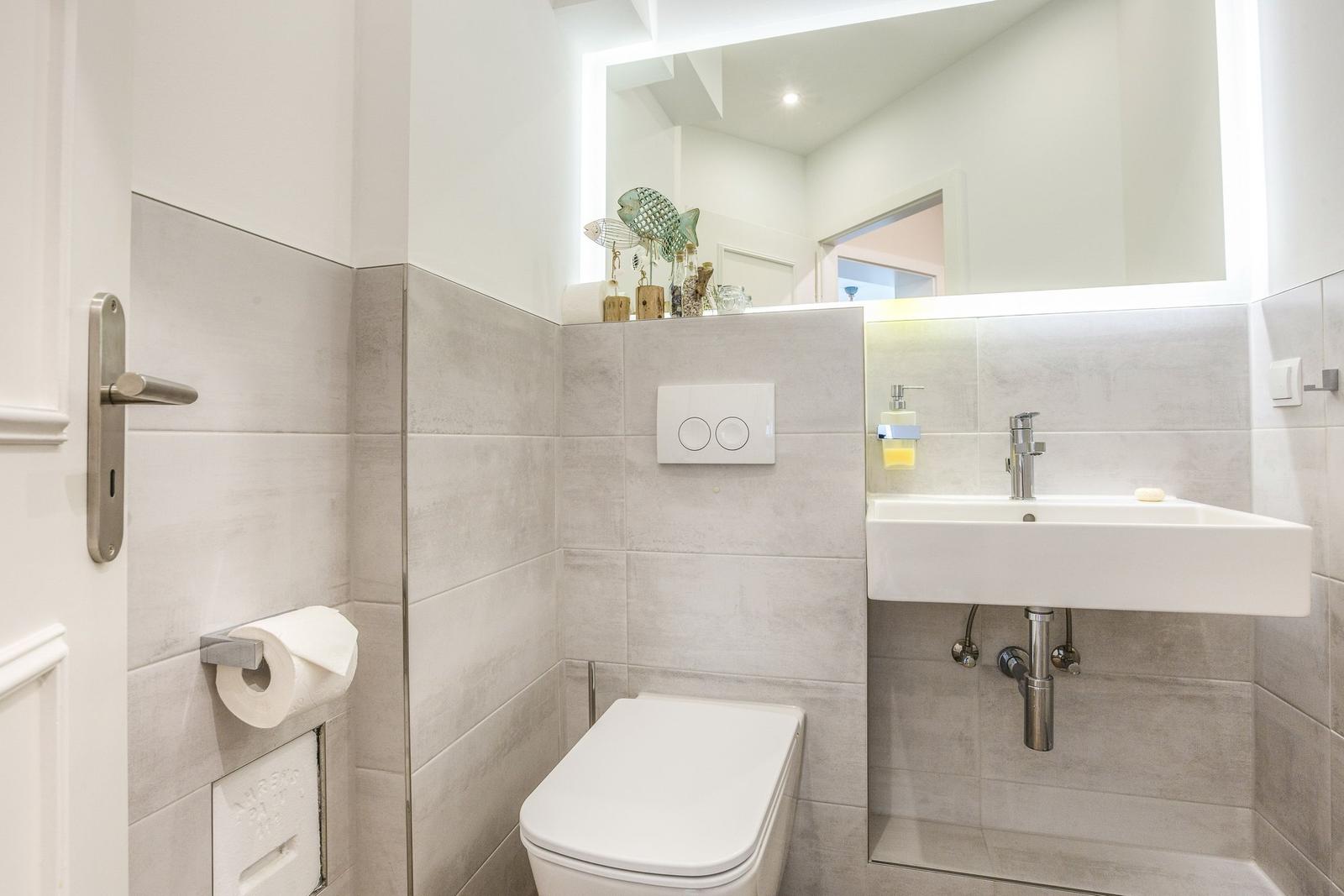 Bathroom with toilet, sink, and lit mirror.