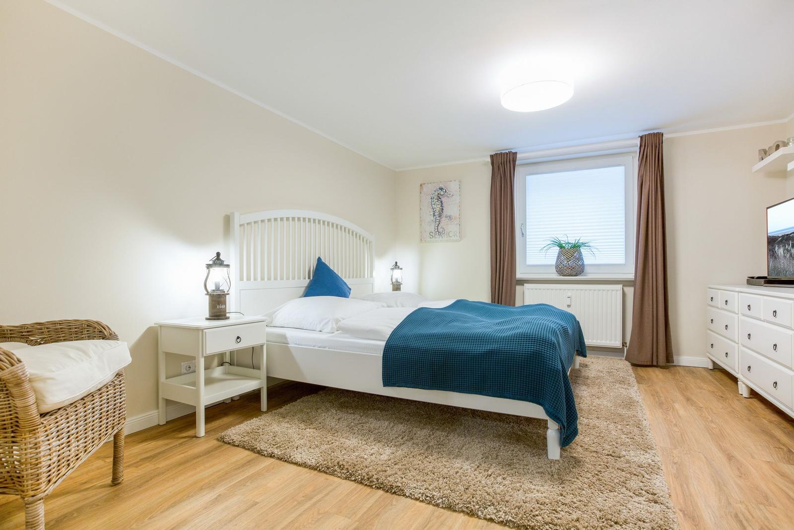 Bedroom with white bed, blue blanket, desk and TV.