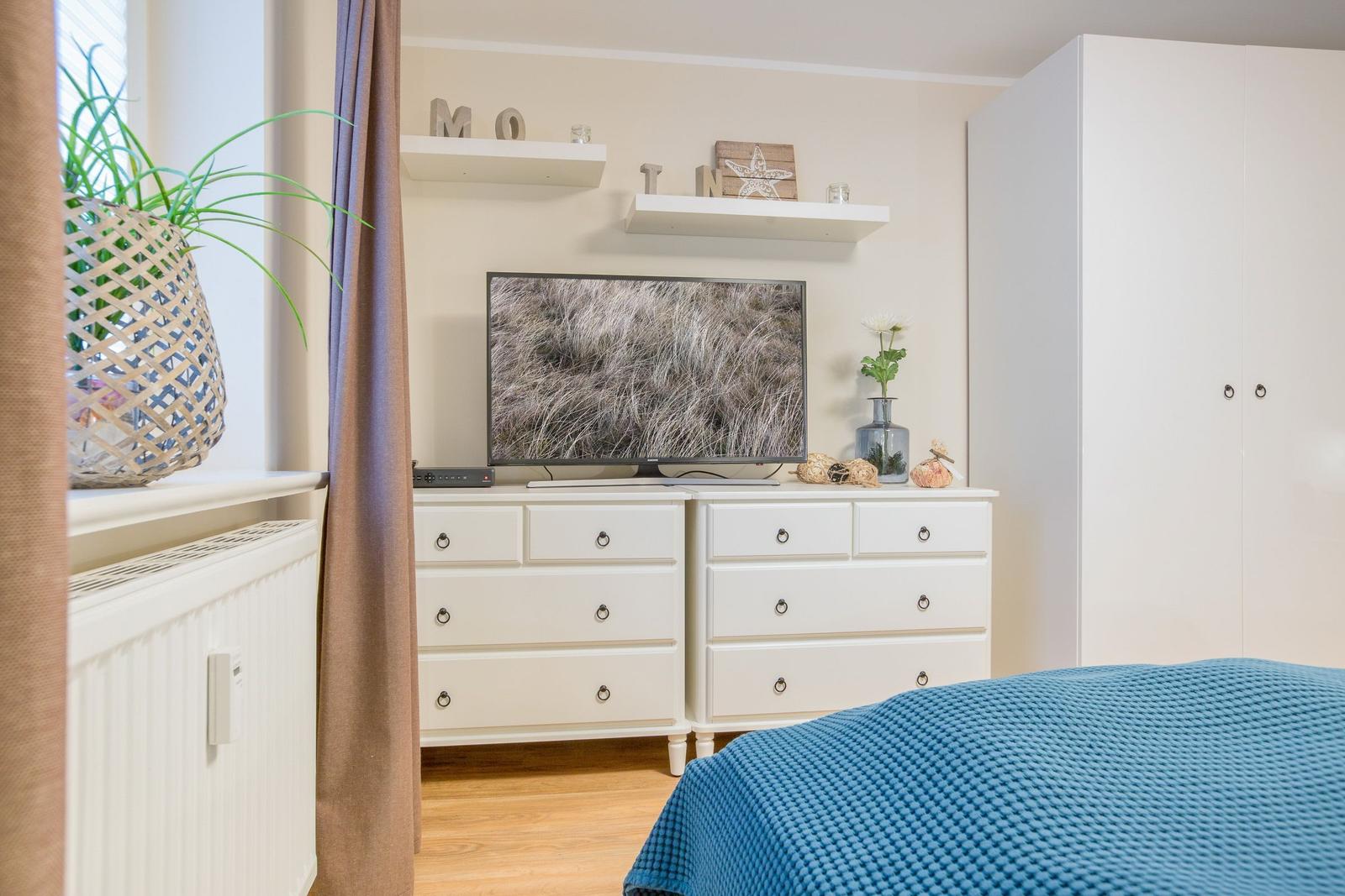 Bedroom with white wardrobe, TV, and plant on windowsill.