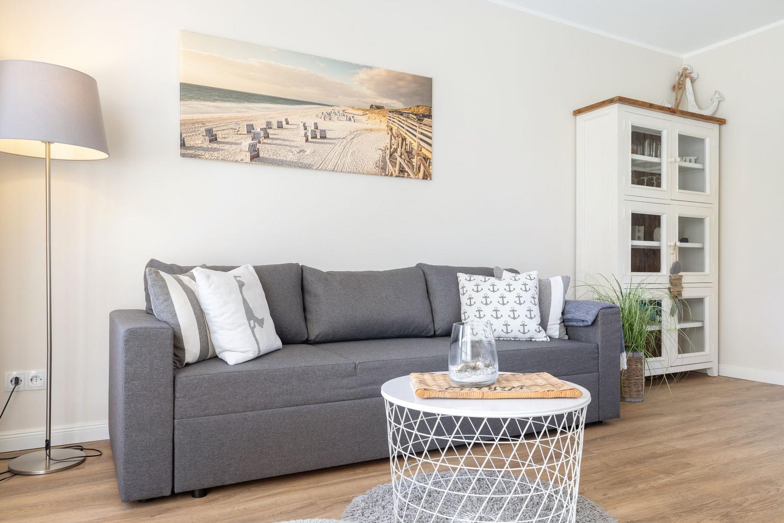 Living room with gray sofa, white table, and beach wall picture.
