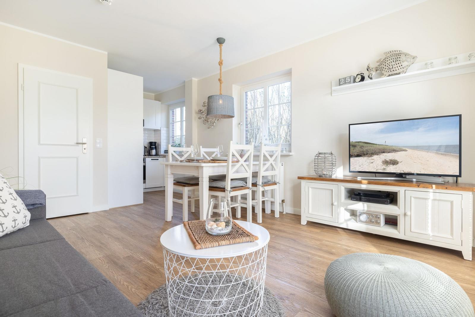 Living room with dining area, TV, and kitchen. Wooden floor and light walls.