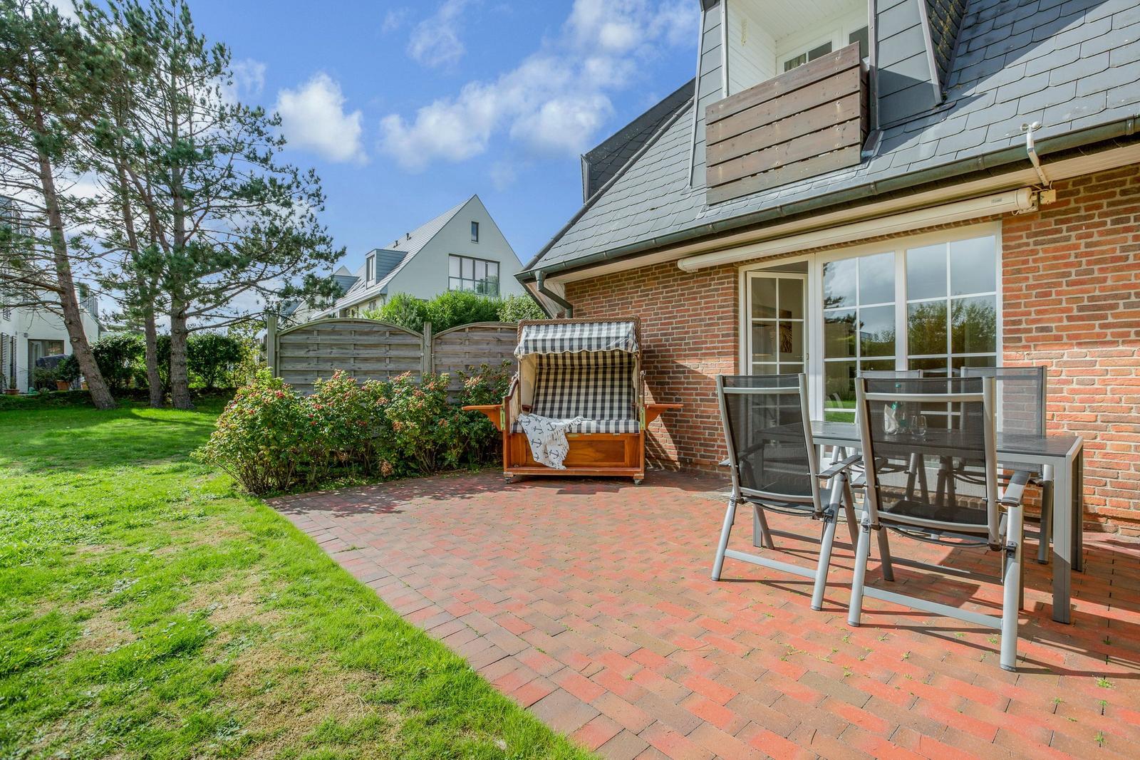 Terrace with wooden lounger and seating group in front of brick house.
