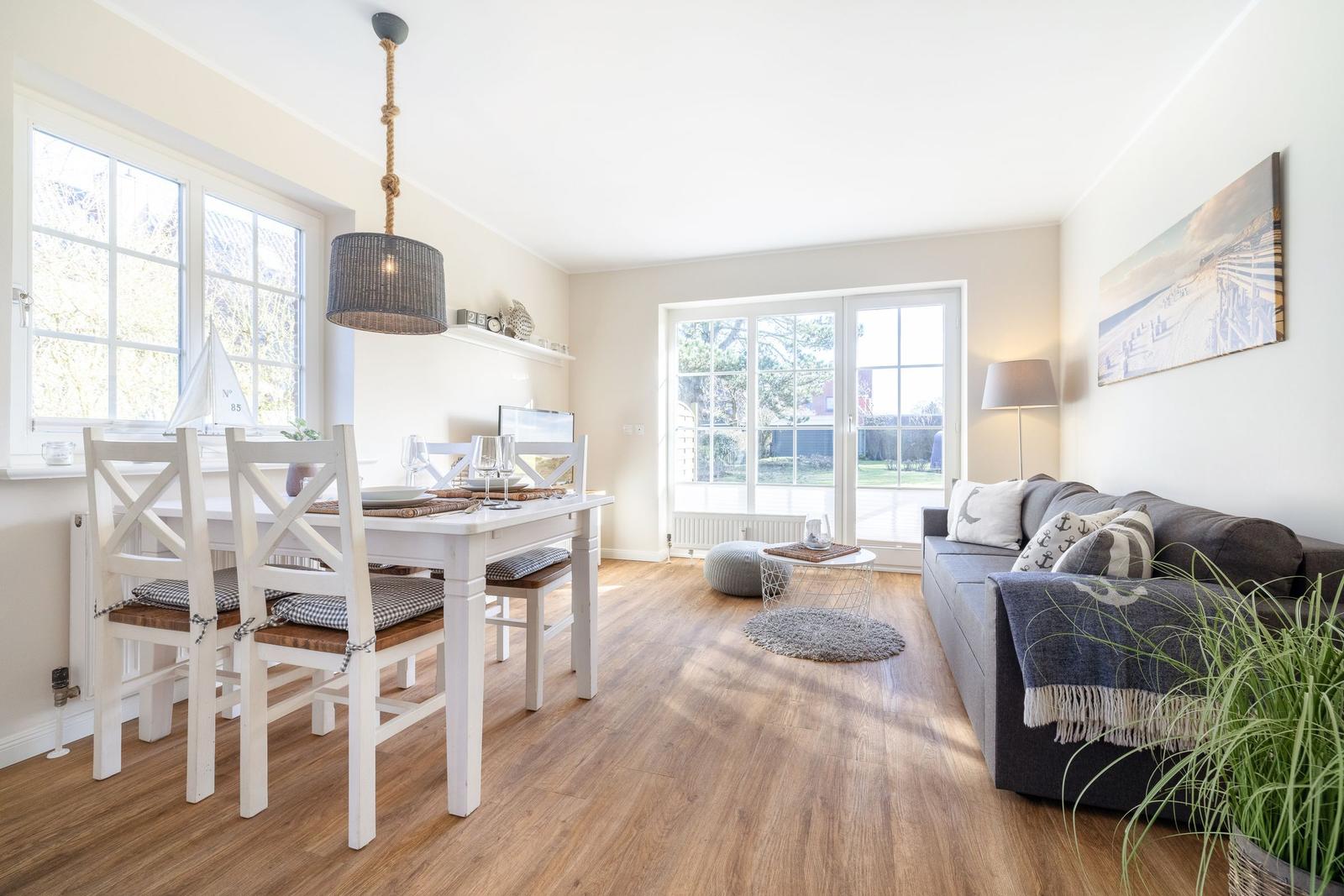 Living and dining area with wooden floor, sofa, table and chairs, and windows.