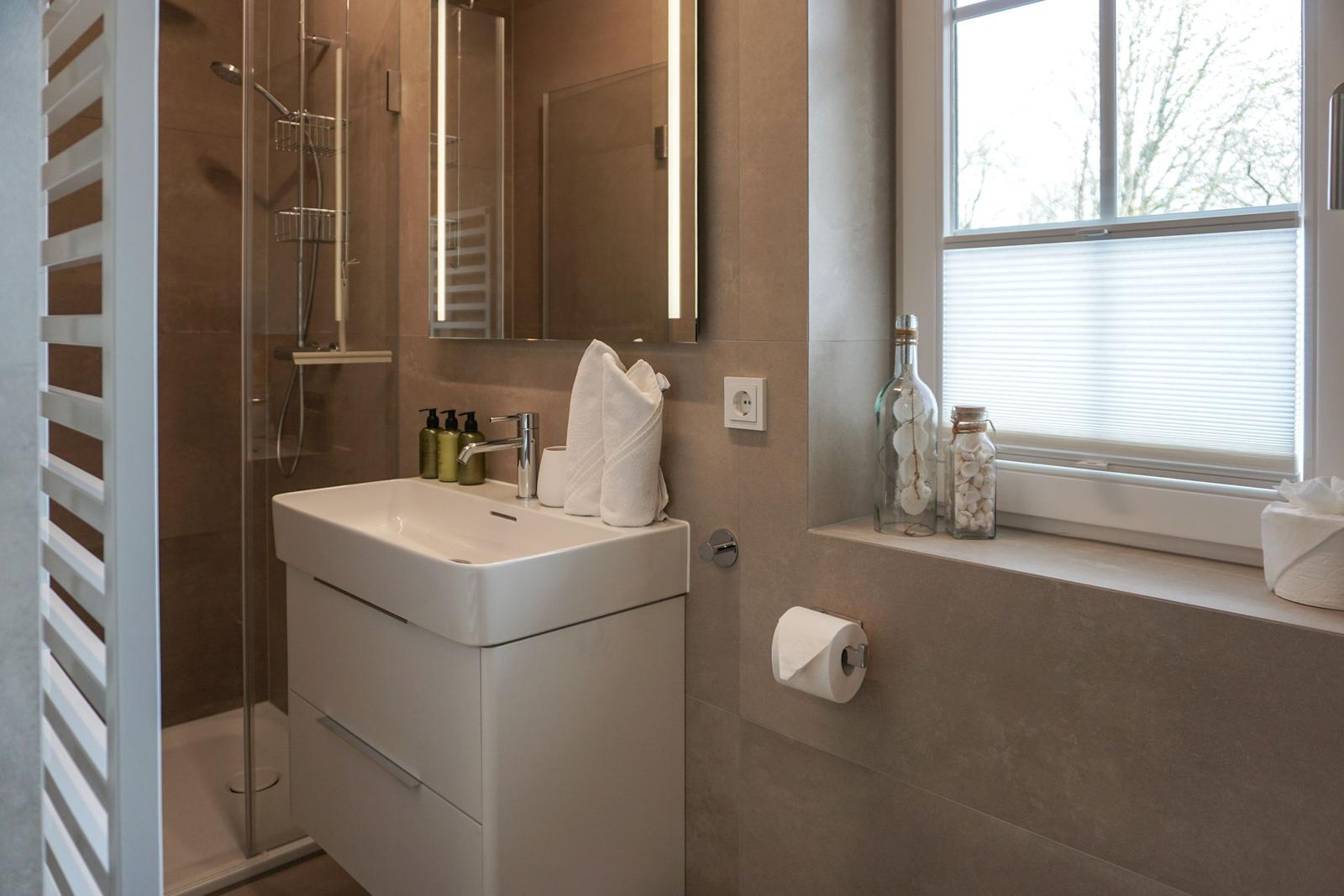 Badezimmer mit Dusche, Waschbecken und Fenster.
