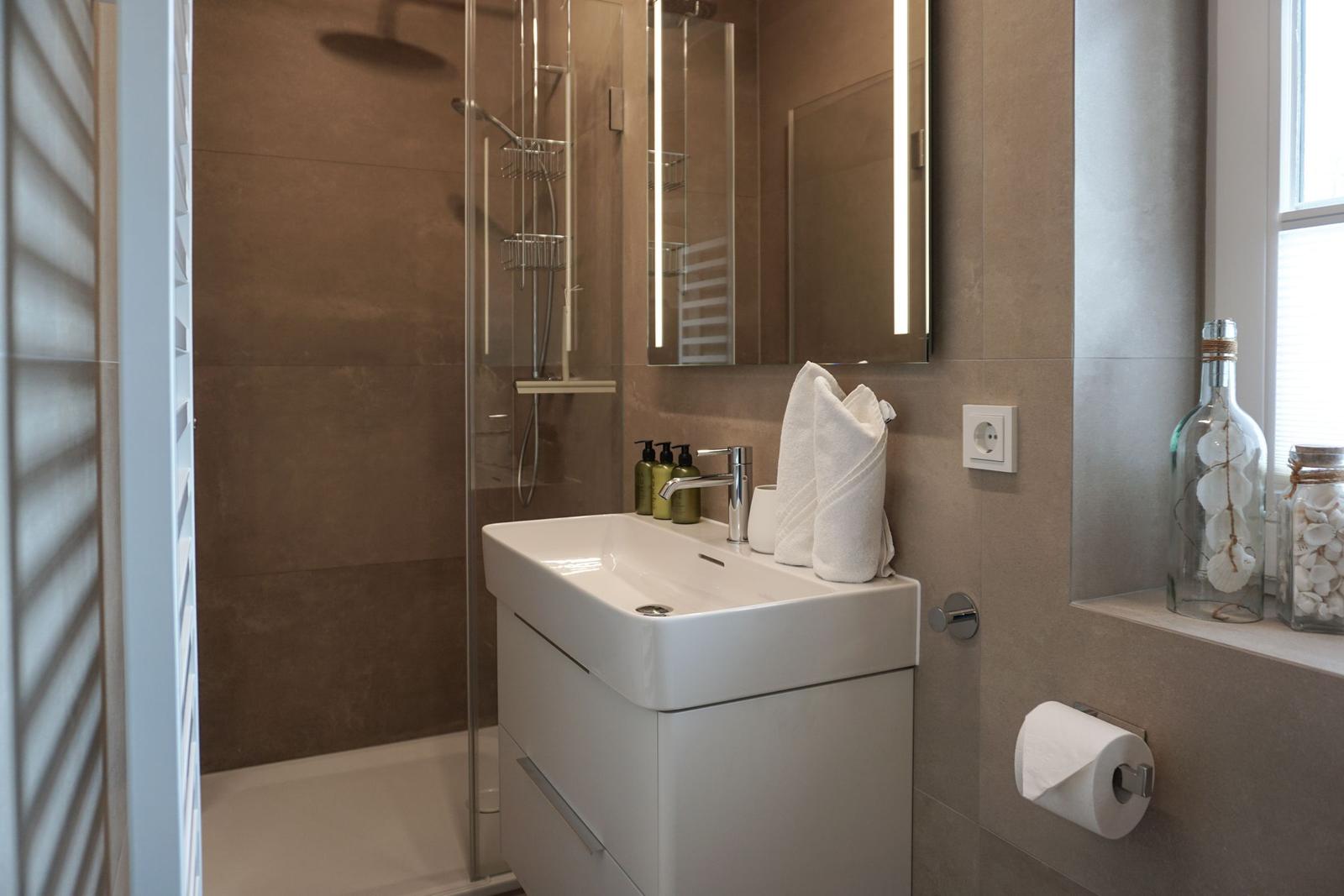 Badezimmer mit Dusche, Waschbecken und Spiegel.