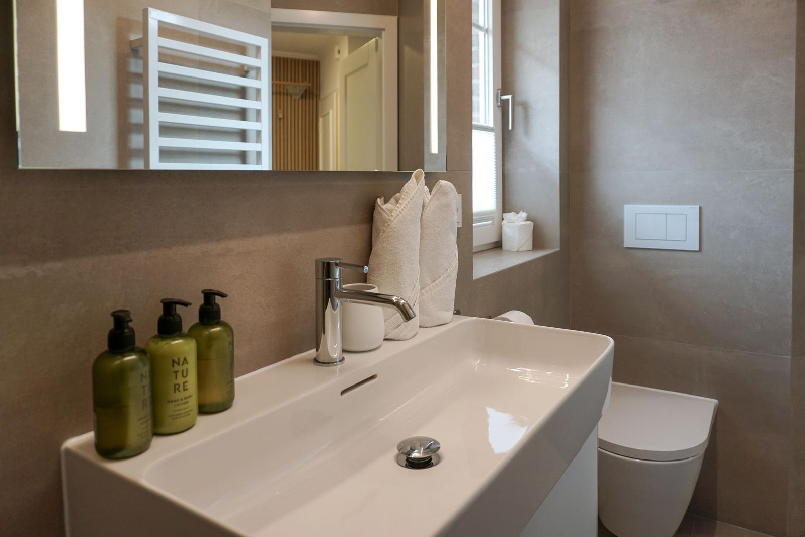Badezimmer mit Waschbecken, Spiegel, Toilette und Handtüchern.