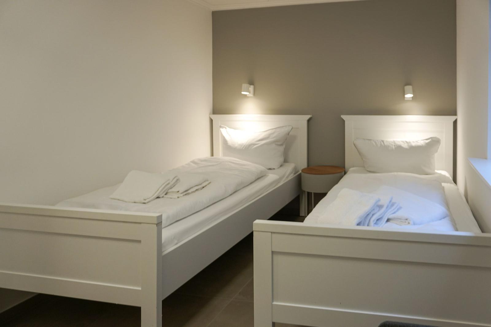 Zwei Einzelbetten mit weißen Laken und Handtüchern. Zwischen den Betten steht ein kleiner Tisch.