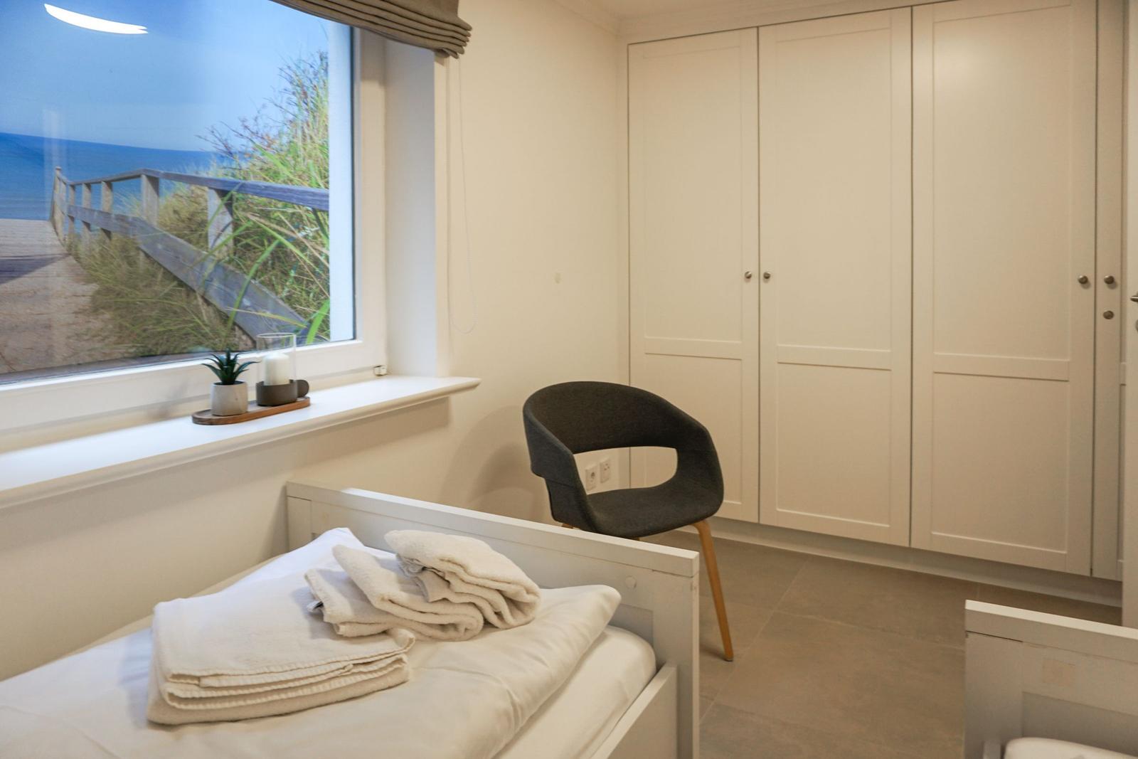 Schlafzimmer mit Blick auf Strand, Bett, Stuhl und Schrank.