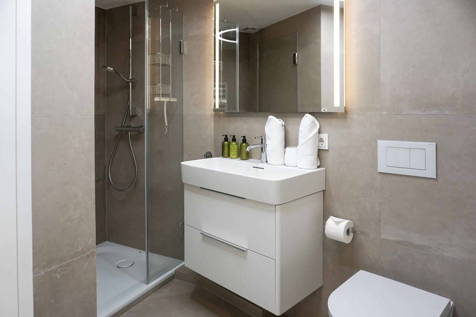 Badezimmer mit Dusche, Waschbecken und Toilette. Fliesenwand und moderne Einrichtung.