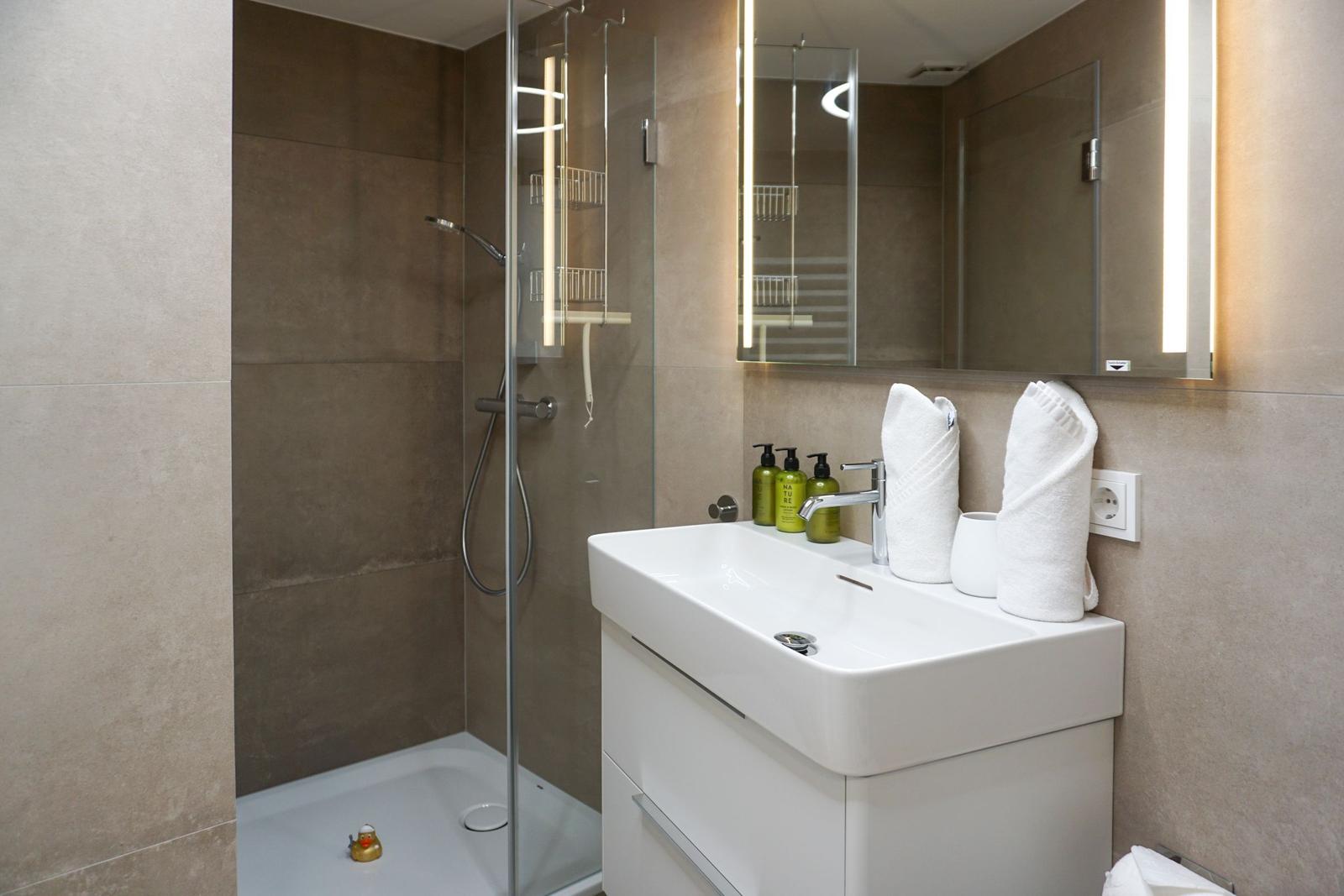 Bad mit Dusche, Waschbecken und beleuchtetem Spiegel
