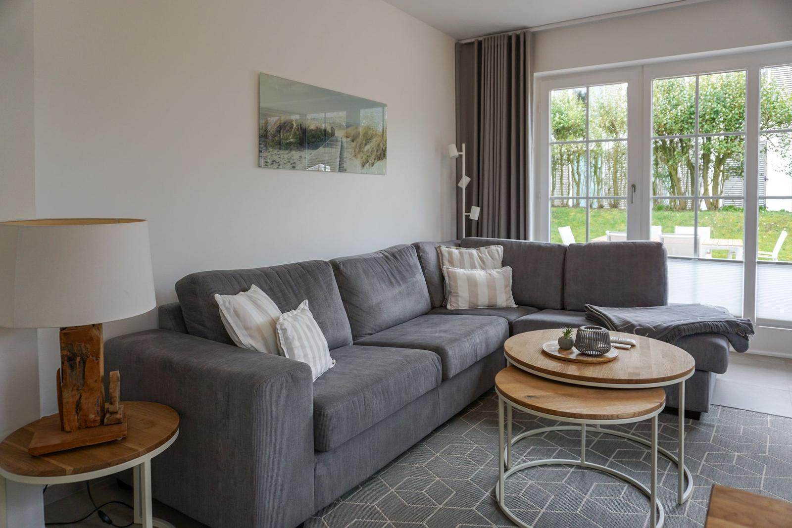 Wohnzimmer mit grauem Sofa, Holztisch und Blick auf Garten.