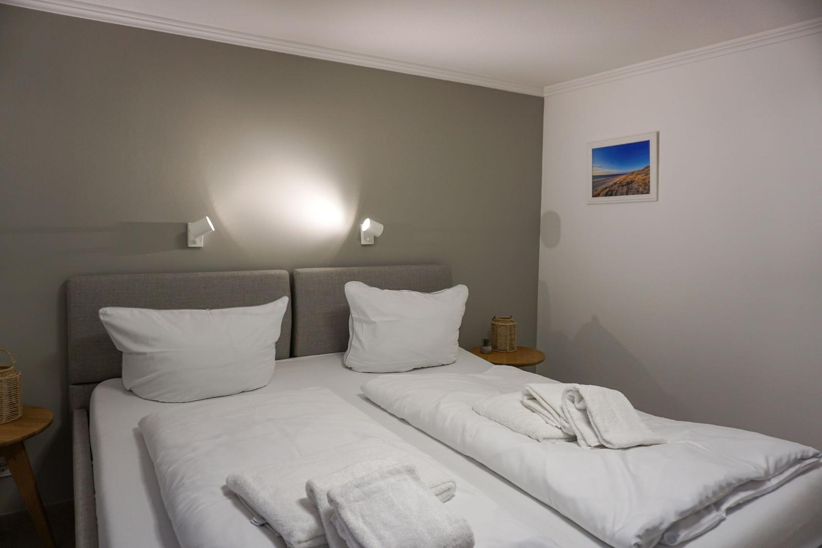 Zwei Betten mit weißen Laken und Handtüchern. Wandlampen und Bild an der Wand.