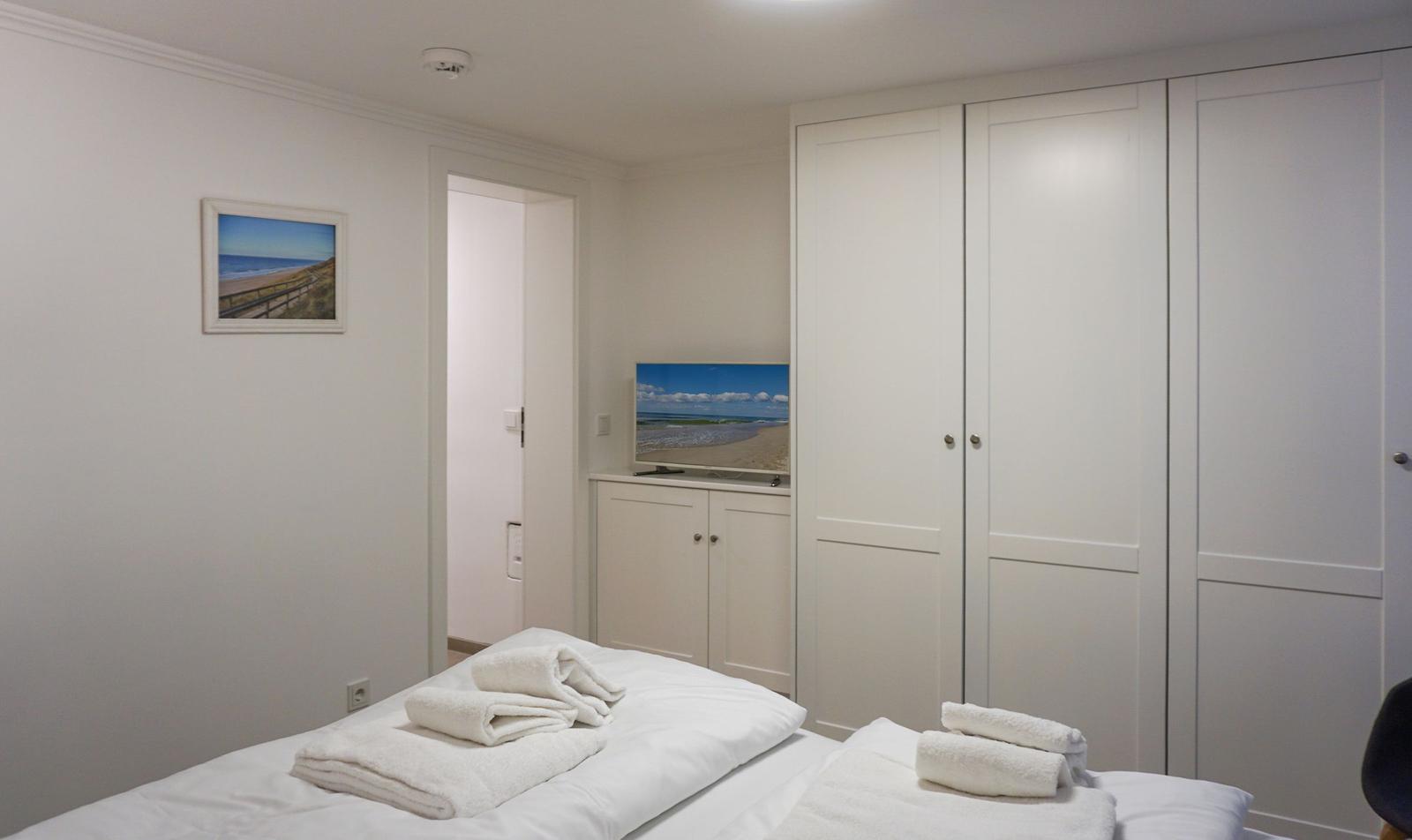 Schlafzimmer mit Bett, Schränken und Fernseher. Wandbild zeigt Strand.