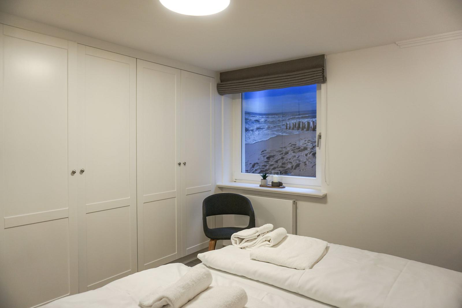 Schlafzimmer mit Bett, Kleiderschrank und Fenster mit Strandbild.