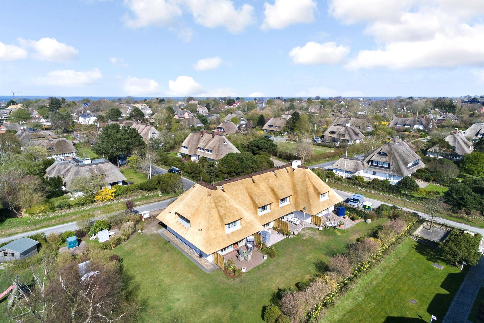 Dorfhaus mit Strohdach, umgeben von Grünflächen und weiteren Häusern.
