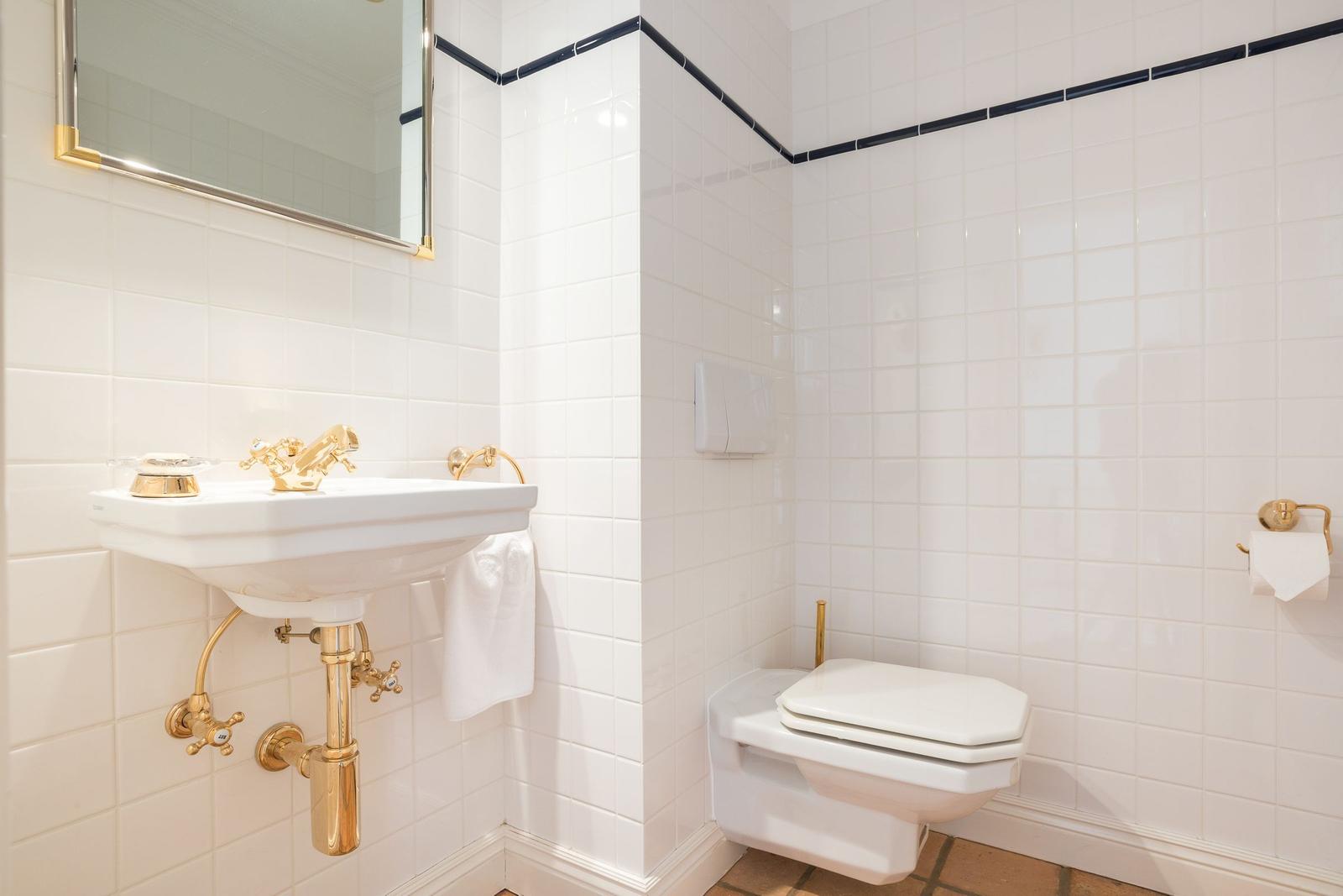 Badezimmer mit weißen Fliesen, goldenem Waschbecken und Toilette.