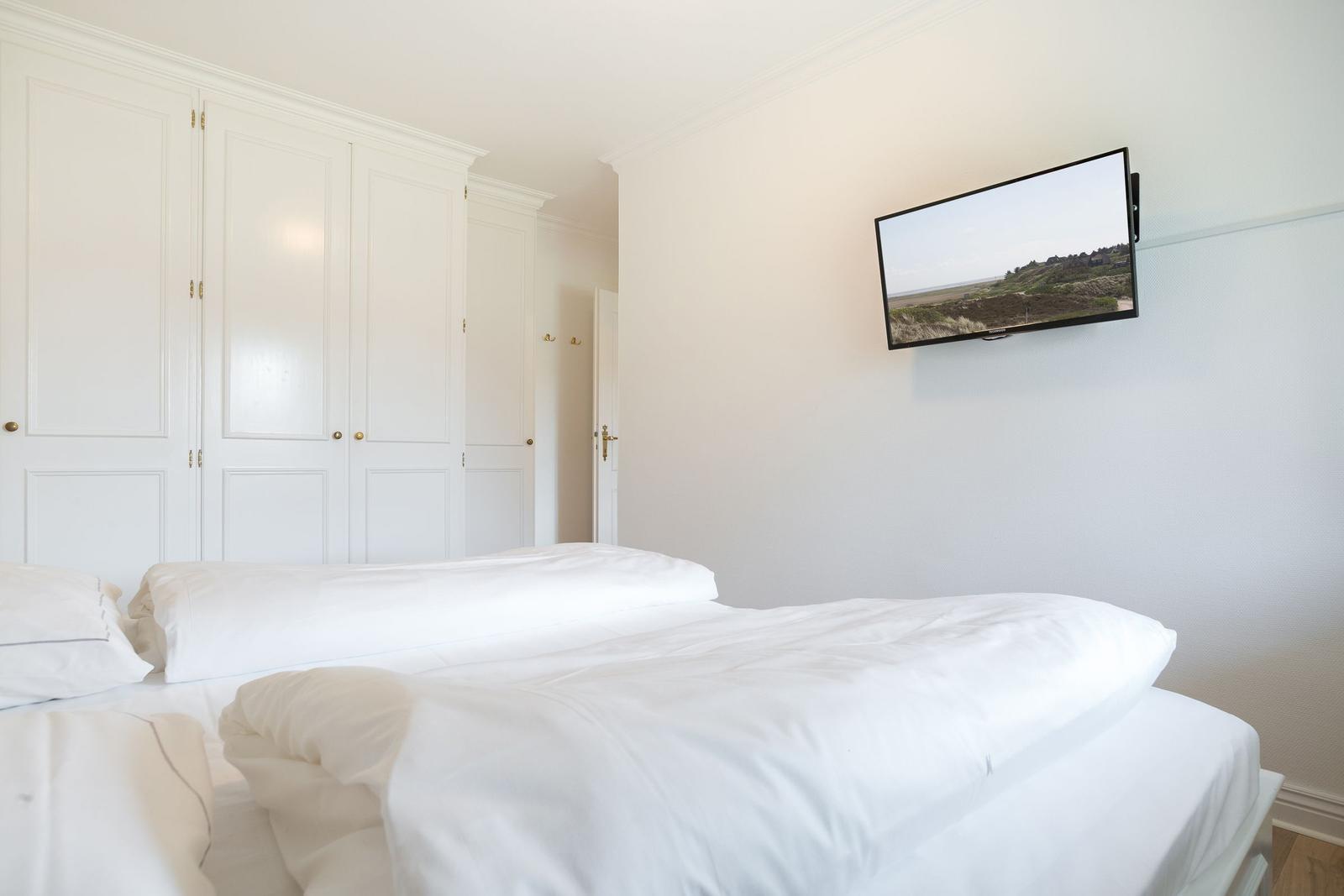 Schlafzimmer mit weißem Bett und Wandfernseher