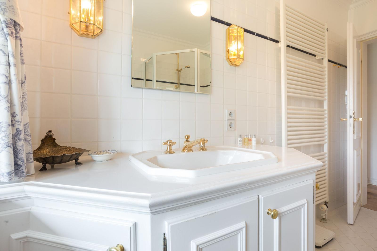 Badezimmer mit weißem Waschtisch, goldfarbenen Wasserhähnen und Spiegel.
