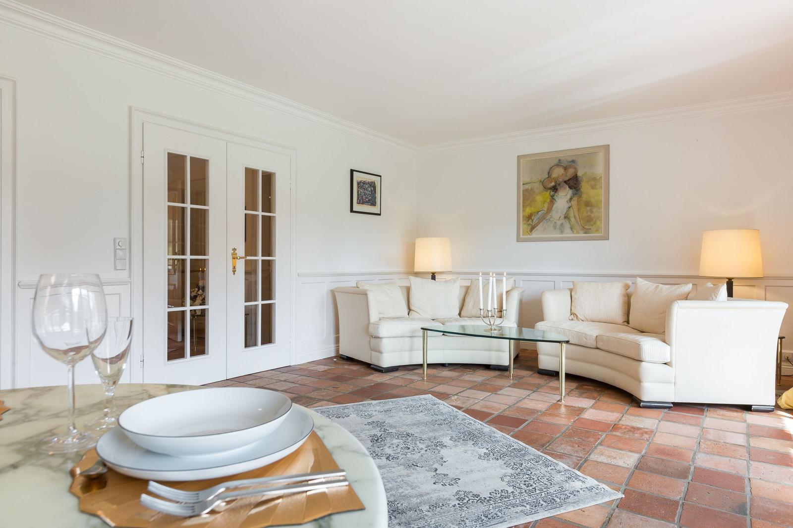 Wohn- und Essbereich mit weißen Sofas, Glas-Tisch und Terrakottaboden.