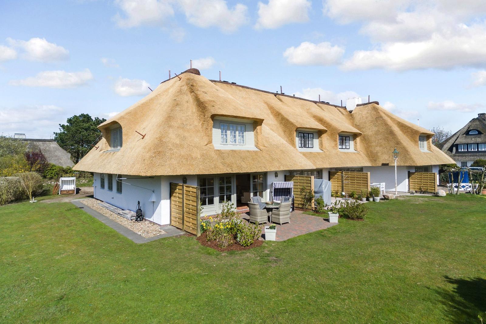 Haus mit Strohdach, Garten und Terrasse mit Sitzgelegenheiten.