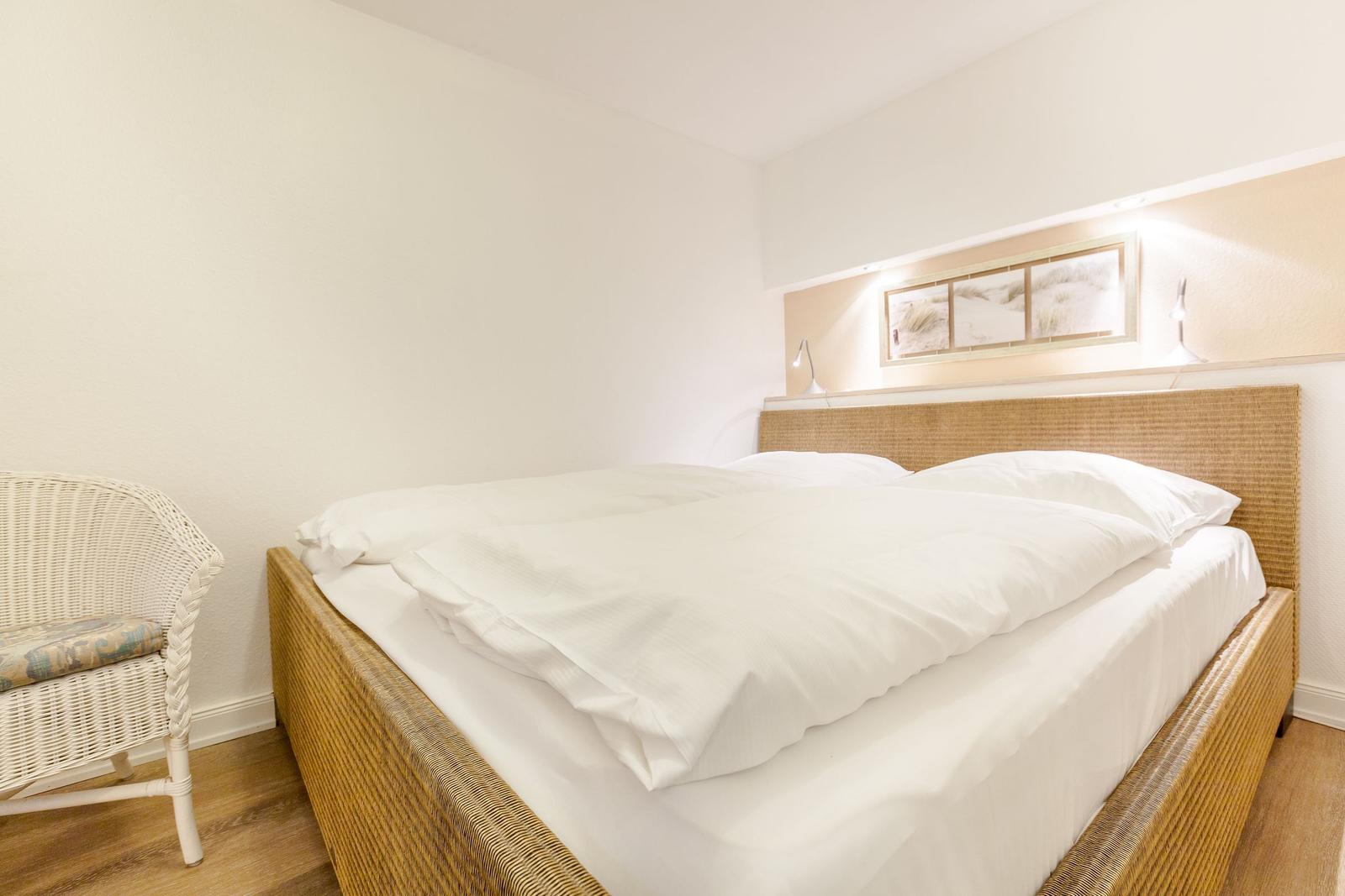 Bedroom with rattan bed, white bedding, and a white chair.