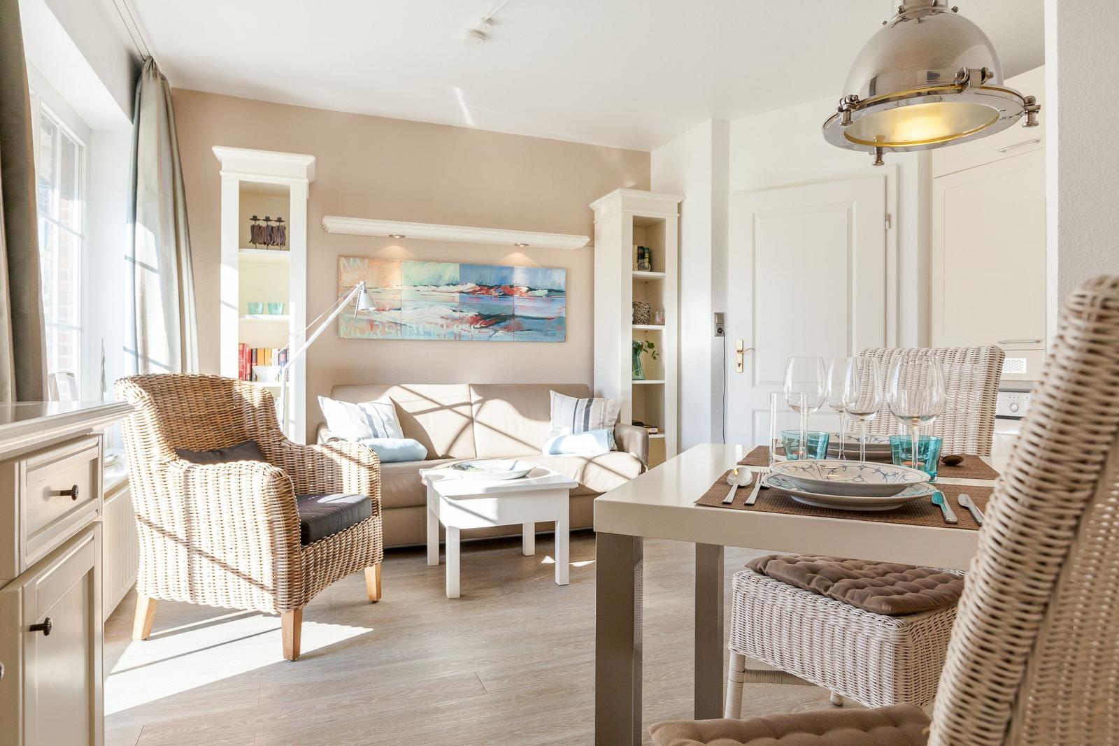 Living and dining area with sofa, dining table, and wicker chairs. Wall art and bookshelves visible.