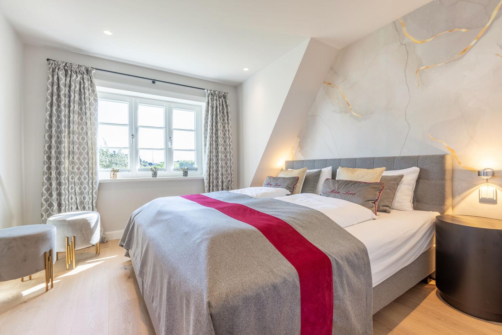 Schlafzimmer mit großem Bett, Fenster und moderner Wandgestaltung.
