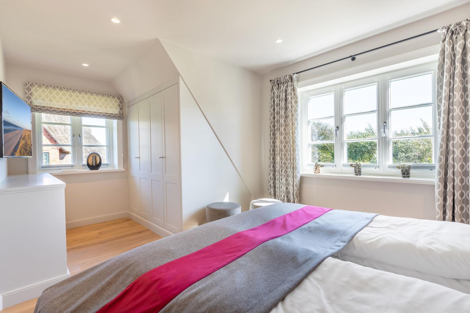 Schlafzimmer mit Dachschrägen, großem Bett und Fenstern mit Blick auf Grün.