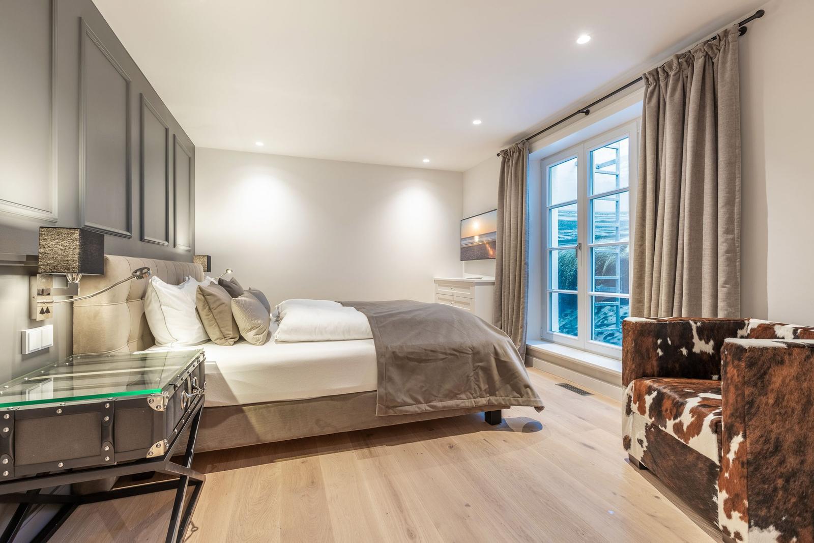Schlafzimmer mit Bett, Fenster und Sessel.