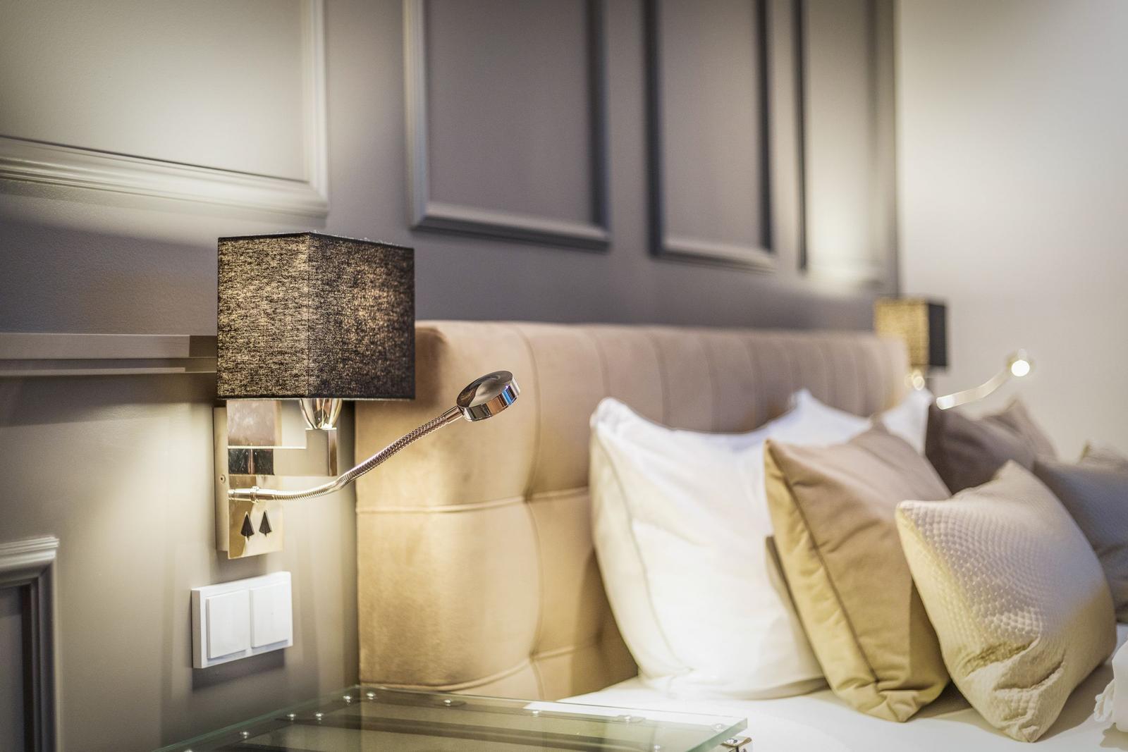 Schlafzimmer mit Beistelltisch, Wandlampe und gepolsterter Kopfseite.