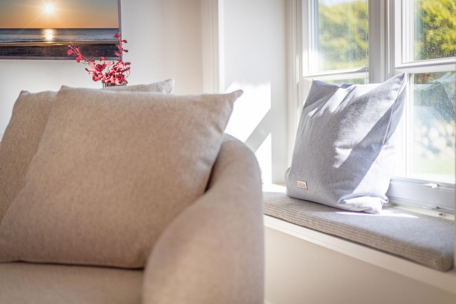 Sofa mit Kissen und Fensterbank mit Kissen und Blumen.